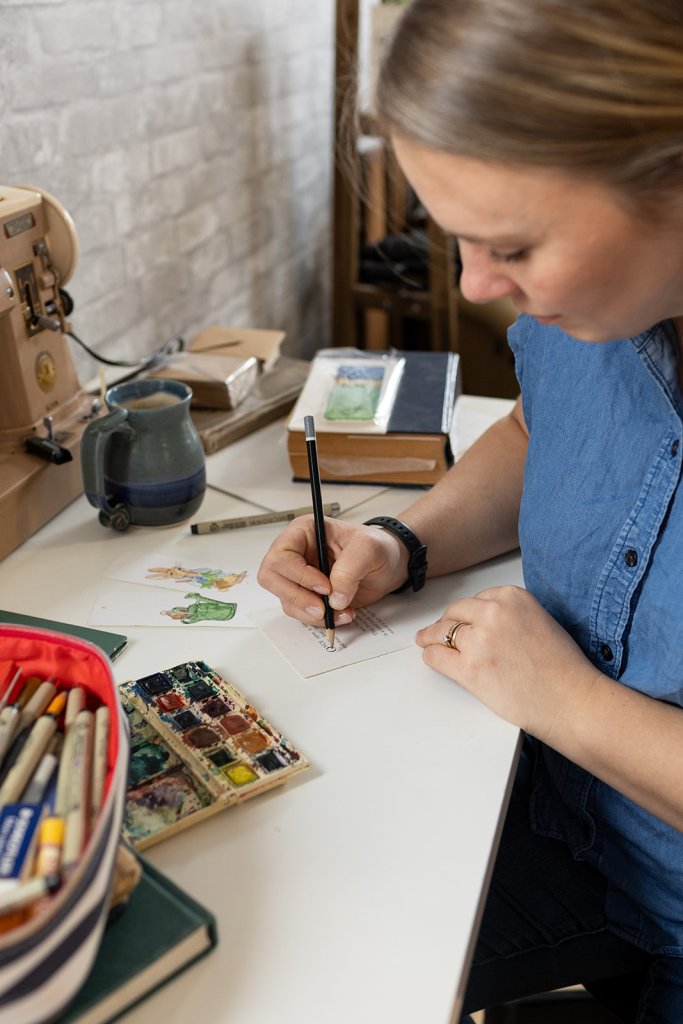 Candid photo of a entrepreneur and artist working at a desk with natural light and personal items

